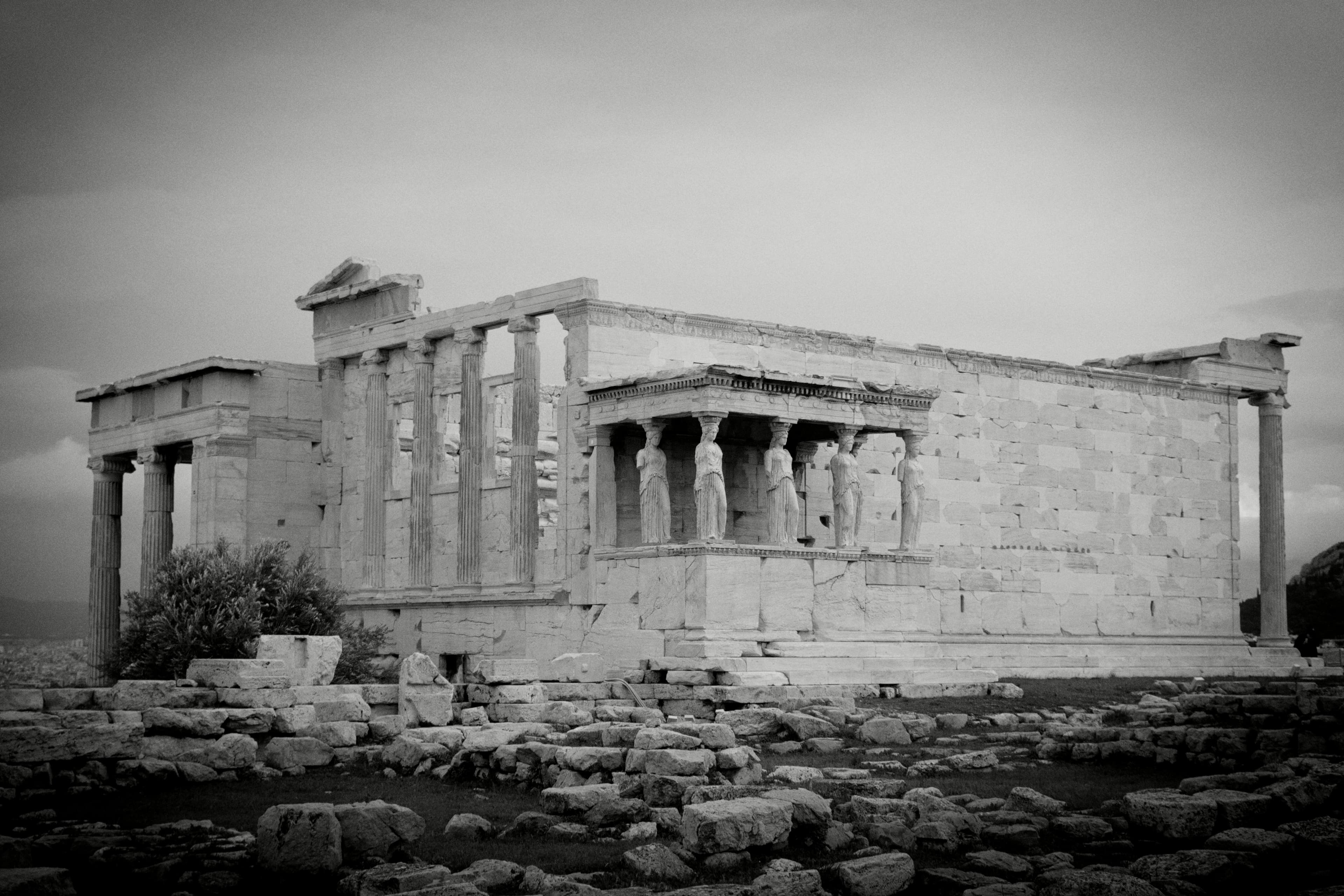 Ancient Greek temple with columns and partially ruined walls on rocky ground, black and white photograph